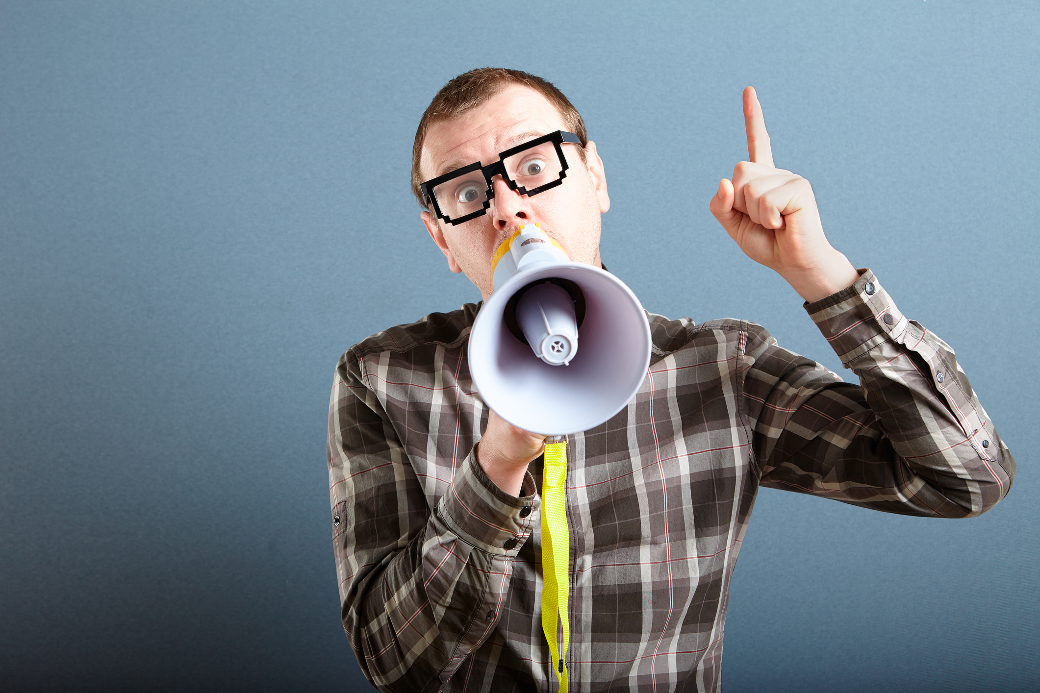 Nerdy guy with glasses holding megaphone and screaming loud, and gesturing with index finger raised