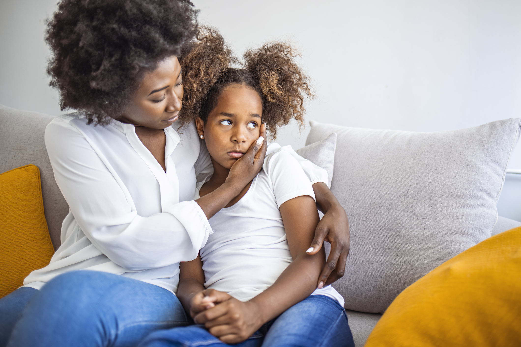 African American mother consoling her sad girl at home. Young black mother taking care of her depressed little daughter at home. Worried young foster mother comforting embracing adopted child daughter