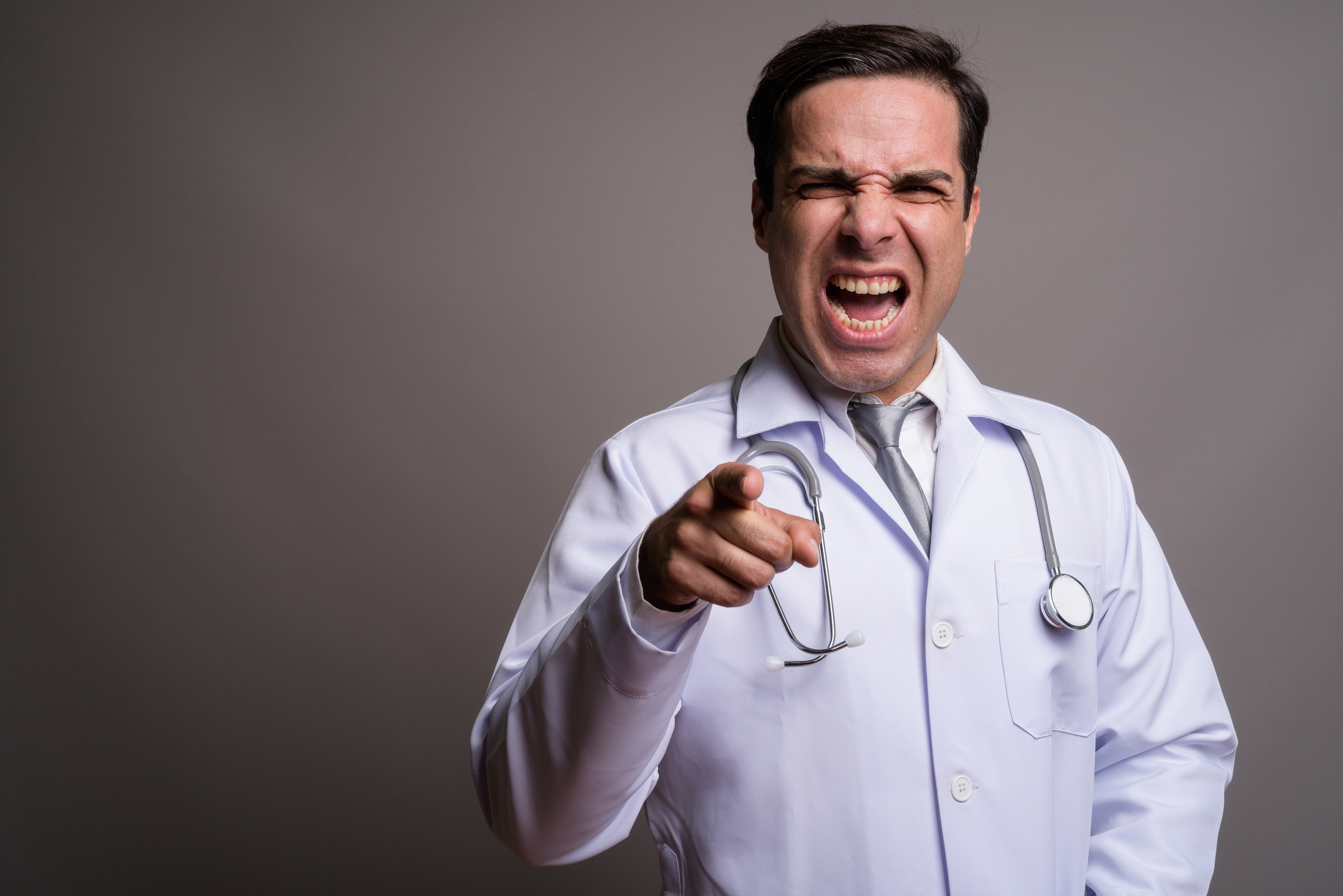 Studio shot of handsome Persian man doctor against gray background horizontal shot