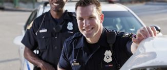 Multi-ethnic police officers (20s) standing in front of police car. Focus on Caucasian man.