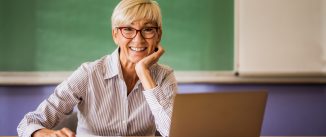 Happy mature teacher at the desk in the classroom.