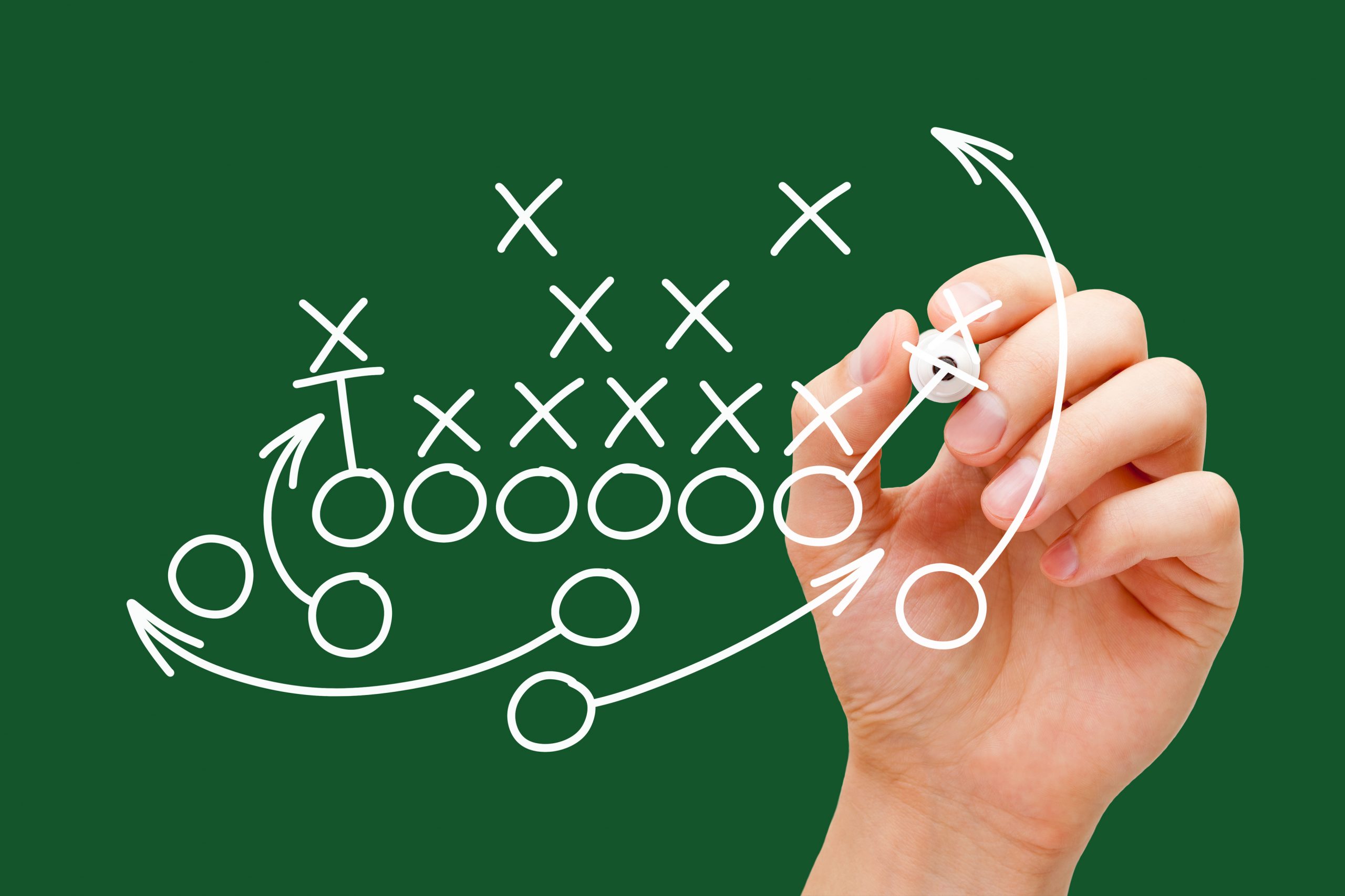 Coach drawing american football or rugby game playbook, strategy and tactics with white marker on green background.