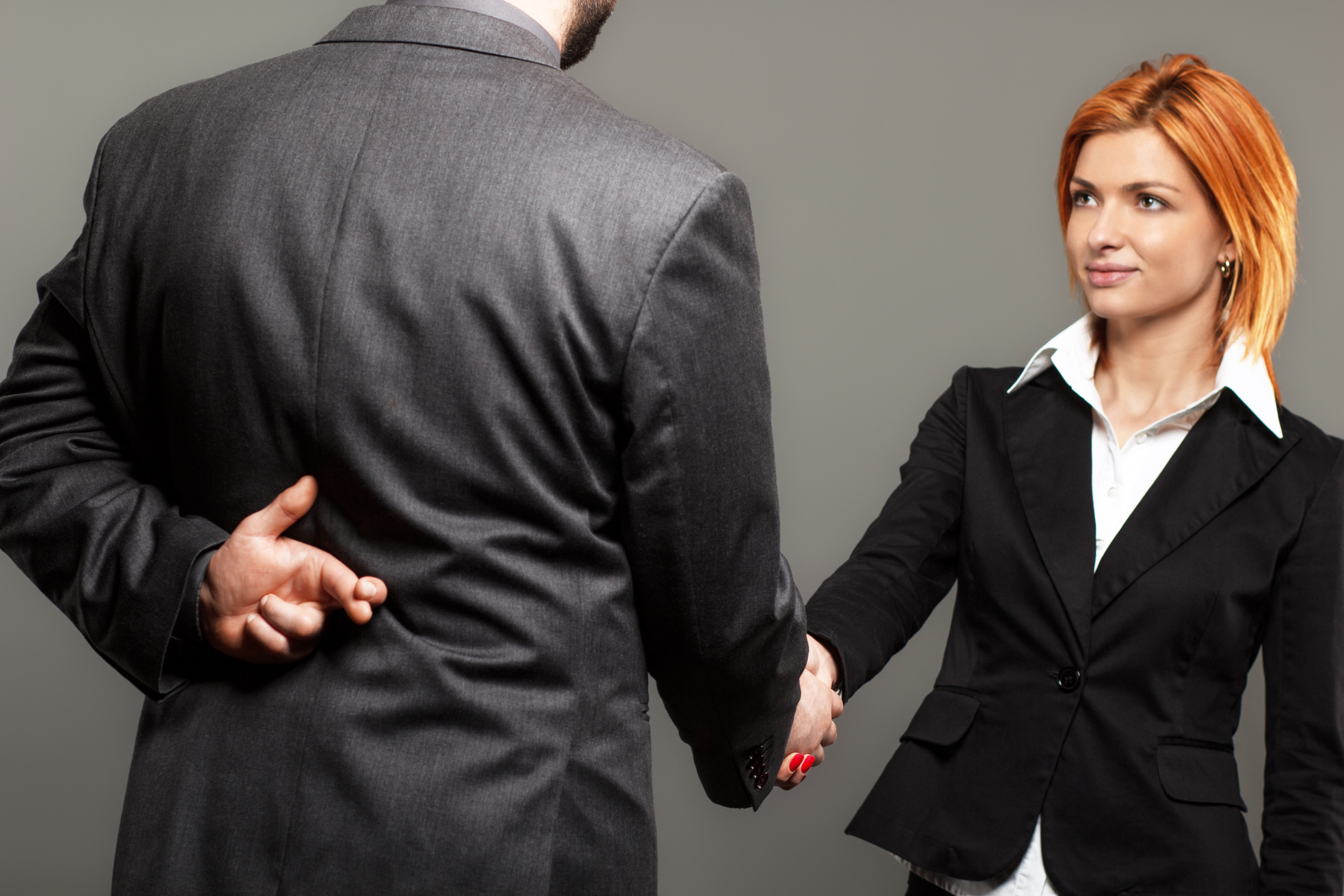 Business partners shaking hands with one of them holding fingers crossed behind back.