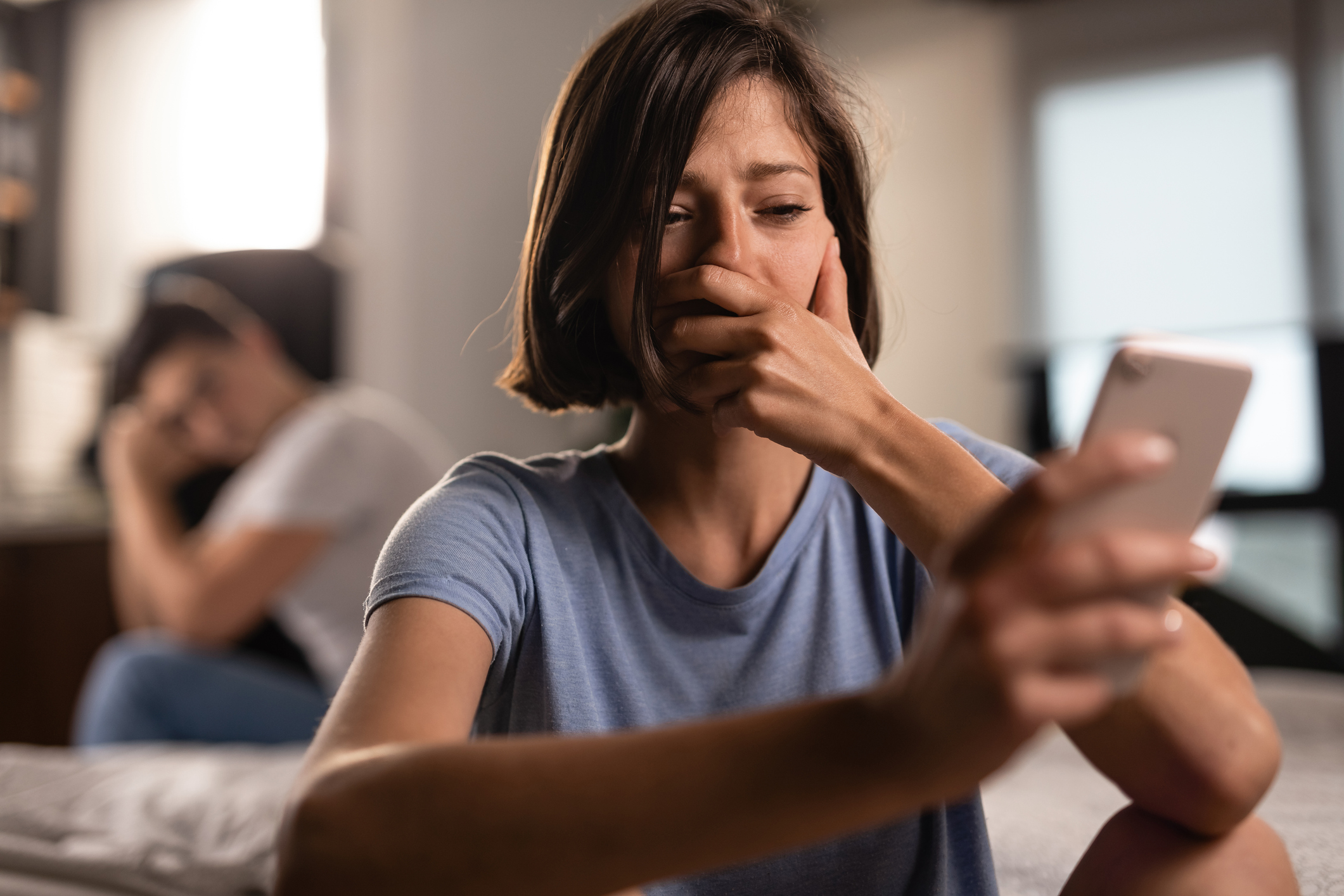 Upset woman reading text messages on her phone. Her boyfriend is in the background.