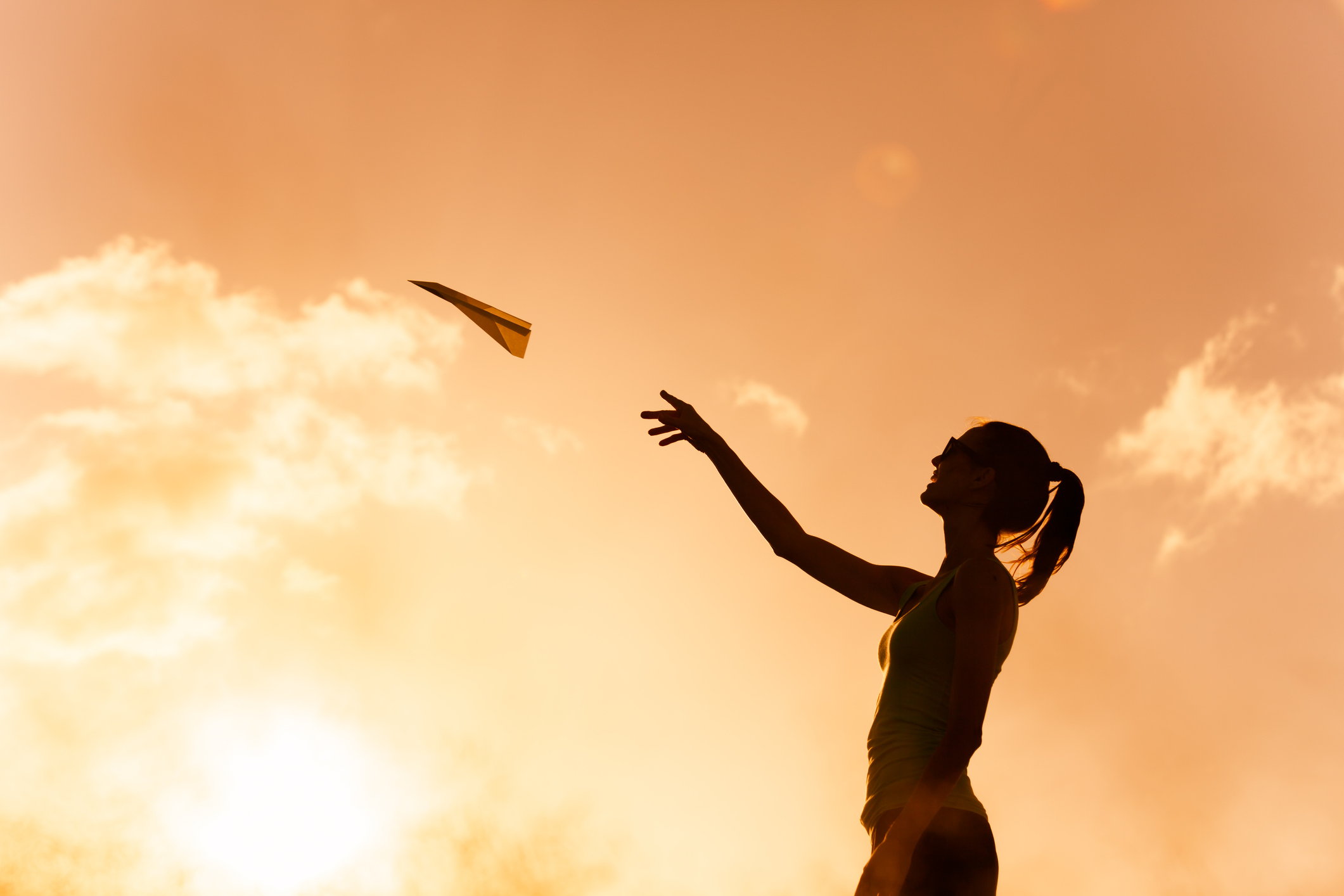 Silhouette of woman throwing paper plane in the park.