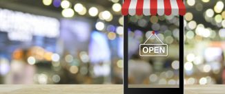 Modern smart mobile phone with on line shopping store graphic and open sign on wooden table over blur light and shadow of mall