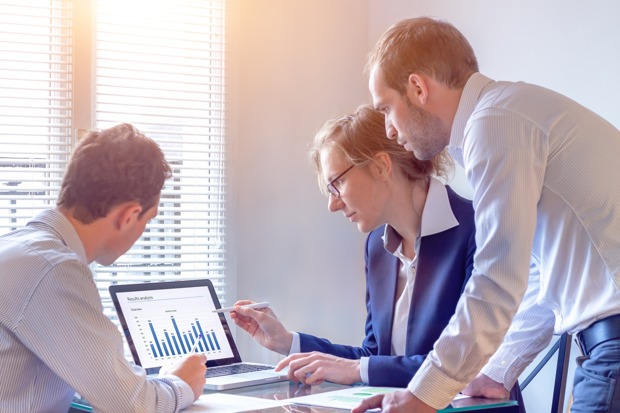 Businesspeople discussing report data with chart on computer screen in office