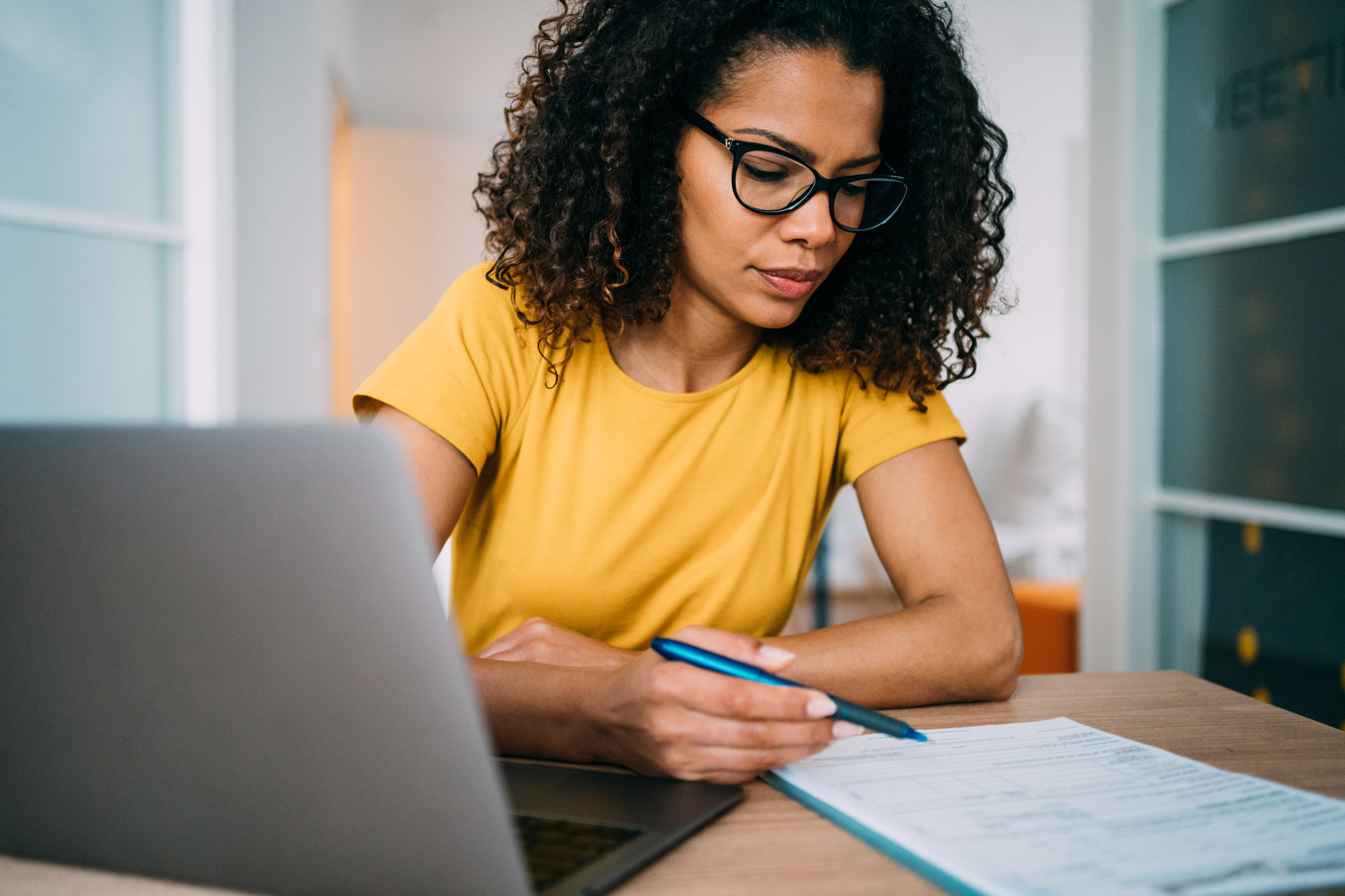 Shot of an adorable african-american businesswoman using laptop and making notes on a clipboard inside of the office.