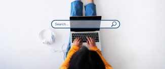 View from above of a woman sitting on a white floor typing into her laptop with a search bar superimposed over the top of the image.