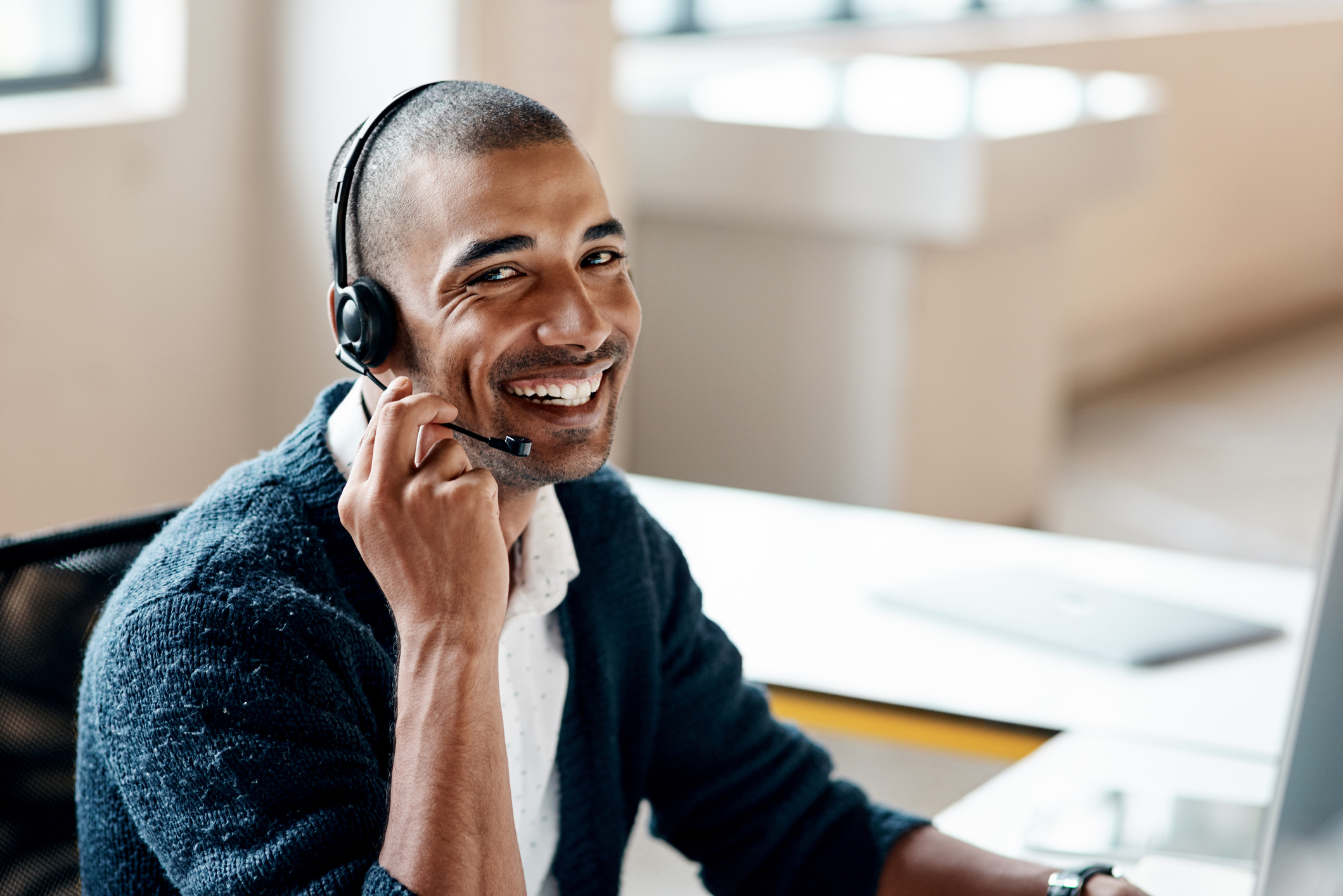 Smiling young man with a business headset on seated in front of a computer in a workplace.