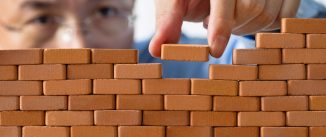 Businessman putting toy brick onto a wall.