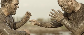 Two men covered in mud face off on a muddly field.