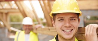 Builder And Apprentice Carrying Wood On Construction Site