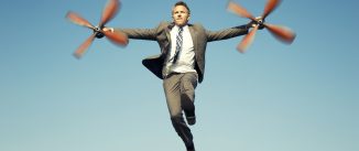 Businessman adventurer holds a set of spinning airplane propellers getting ready to fly in blue sky